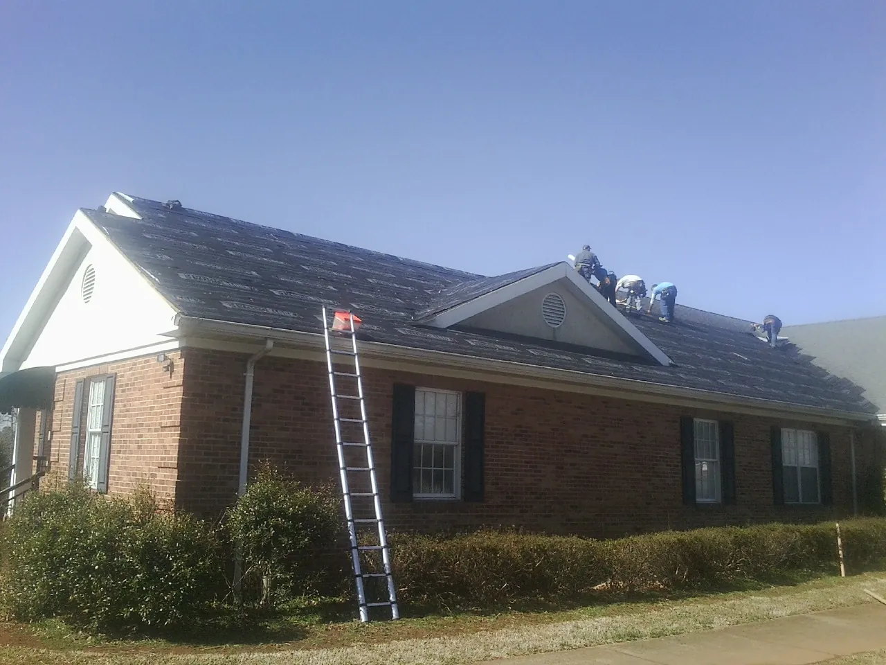 Crew tearing shingles off a brick ranch roof with a ladder set — Metal Roof Repair work by our crew in Middlefield