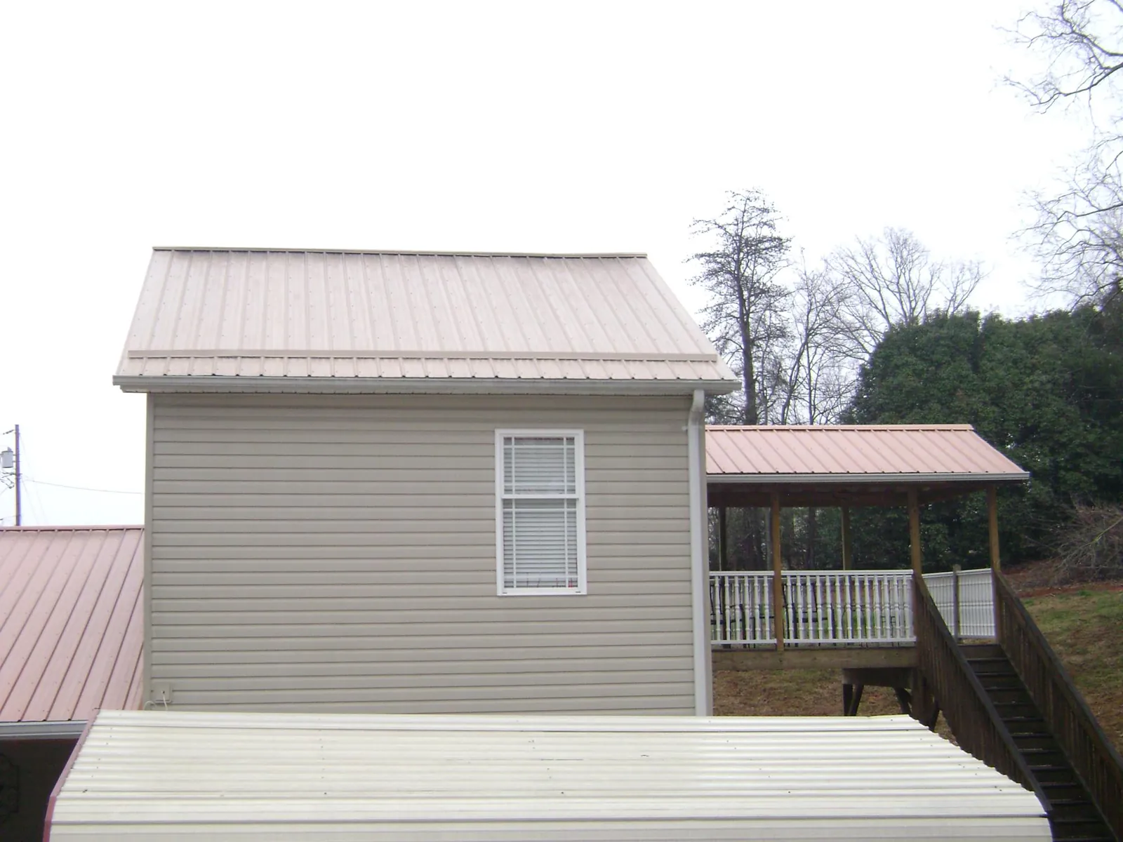 Tan metal roofs on a two story addition and attached porch, from a Roof Replacement job in Middlefield